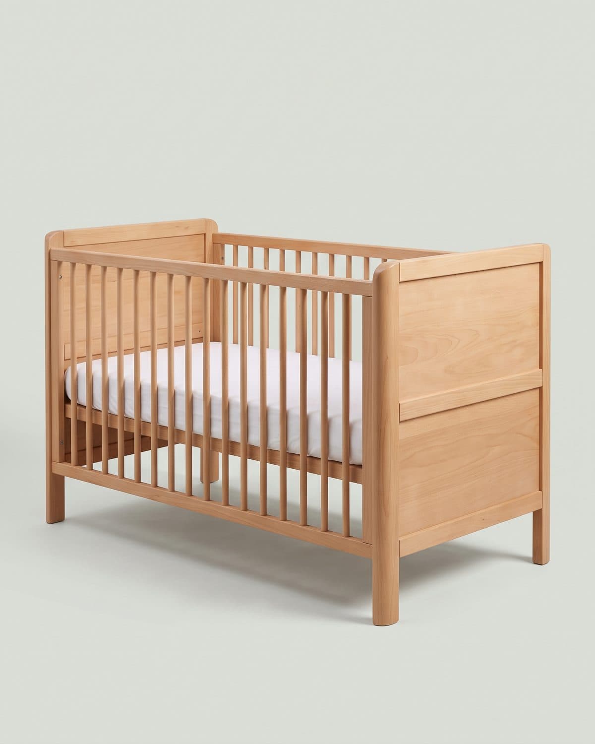 Lit bébé en hêtre massif à barreaux ronds et angles arrondis, drap housse blanc, sur fond sauge pâle